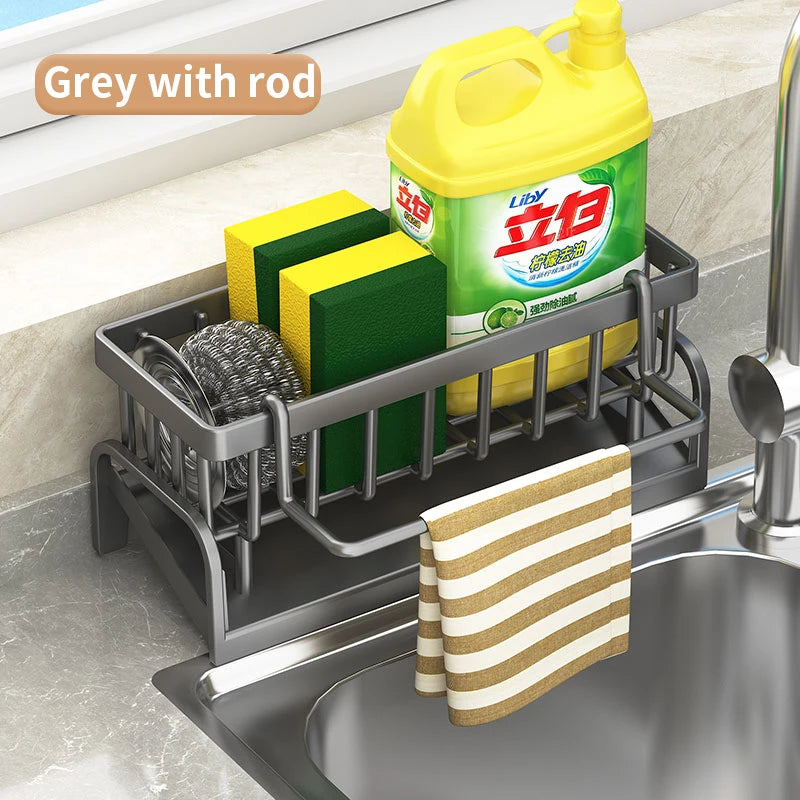 Grey kitchen sink organizer rack with rod holding cleaning sponges, steel scrubber, and detergent bottle
