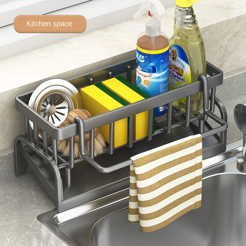 Gray kitchen sink organizer rack holding sponges, brush, spray bottle, and dish soap with towel hanging over sink